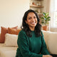 A smiling South Asian parent in a bright, modern home setting, conveying a happy and satisfied customer expression.