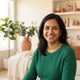 A smiling South Asian parent in a warm, modernly decorated home living room.